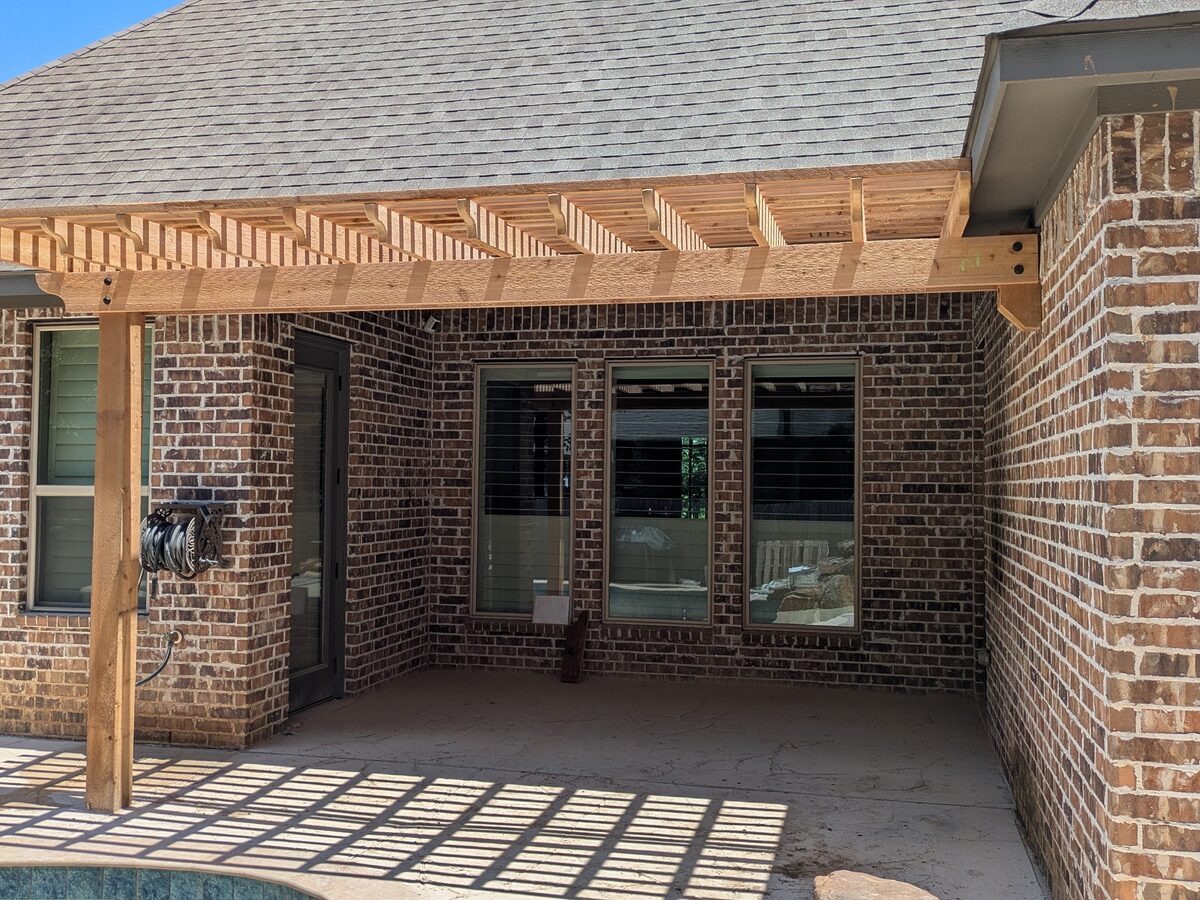 Cedar pergola attached to brick home with slatted shade pattern