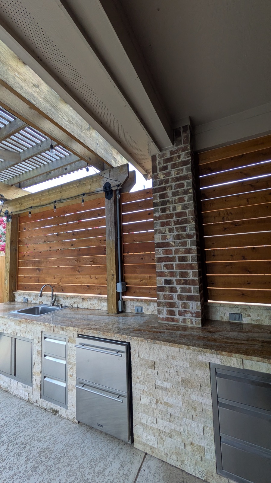 Slatted privacy wall screening behind an outdoor kitchen with pergola overhead